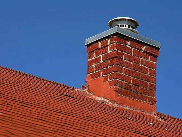 Red brick chimney with a cap on a tile roof